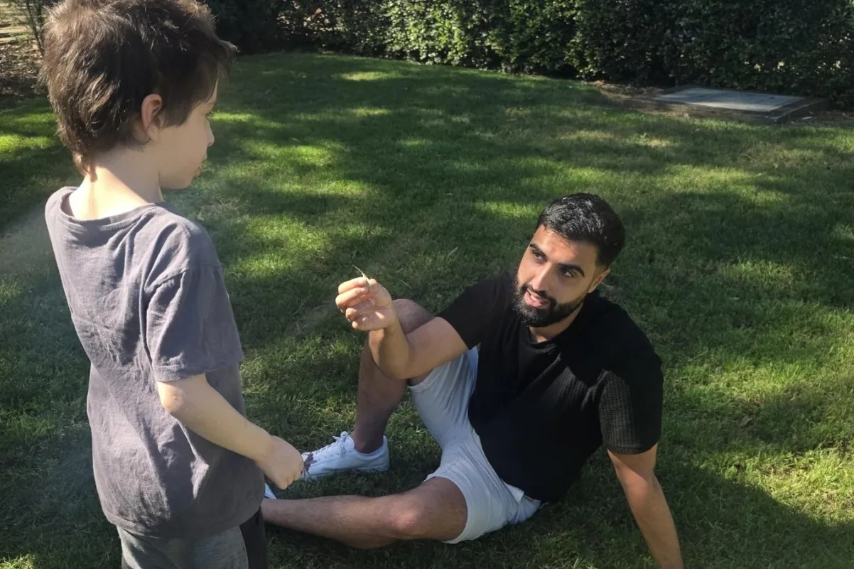 Ali, one of our behaviour support practitioners, sitting on the grass with a child